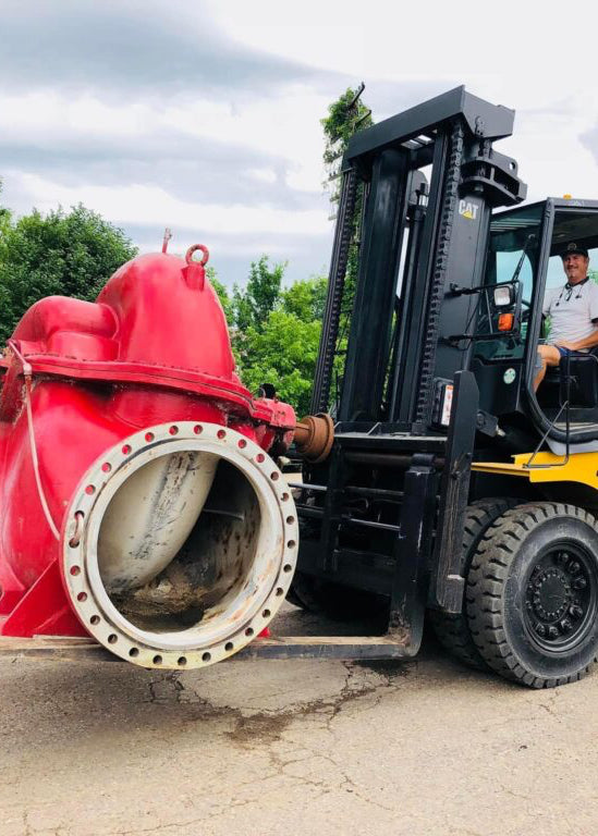 Forklift carrying a large red and white cylindrical object outdoors.